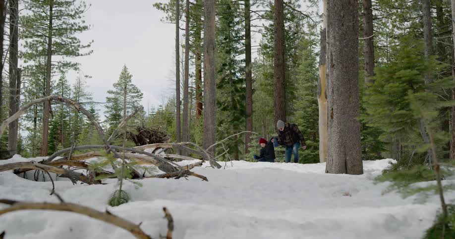 A parent and a child struggle through a forest covered in snow