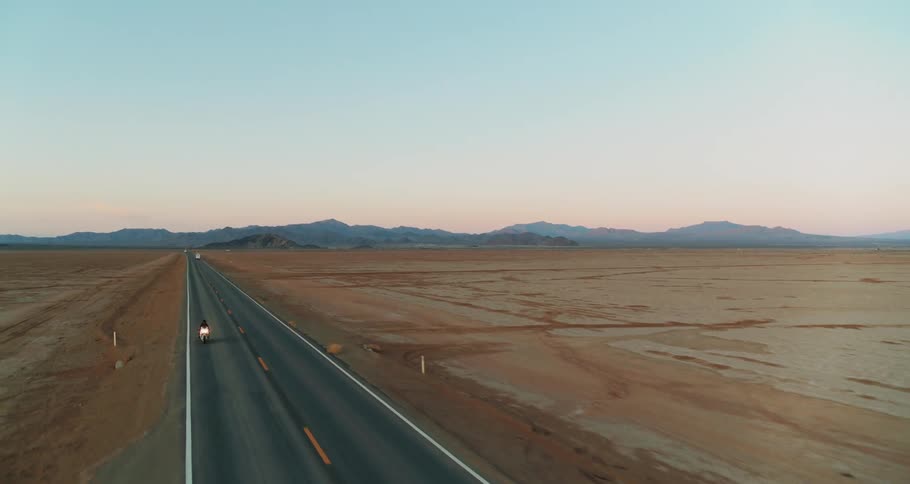 A motorcycle travels on an empty desert road past people and cars parked off road