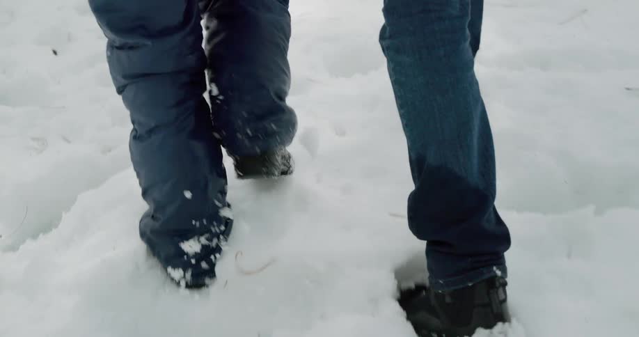 Two people in winter clothing walk across snow covered ground