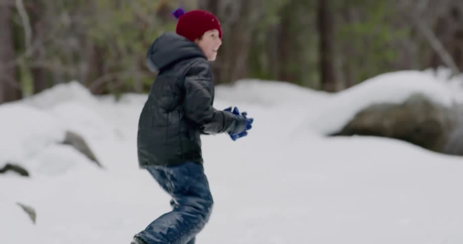 A boy picks up a snowball and throws it at someone who is throwing back at him
