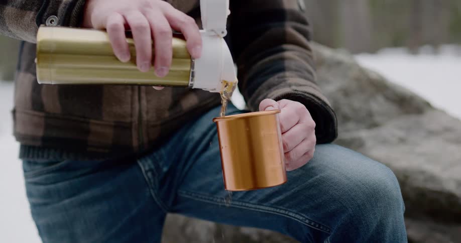 A man pours a cup of coffee by the forest