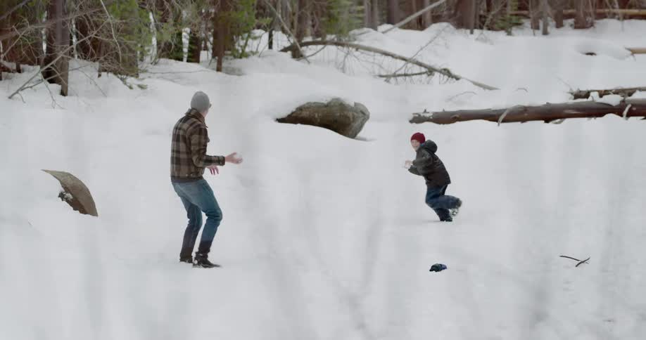 Father and son have a snowball fight outdoors near the woods