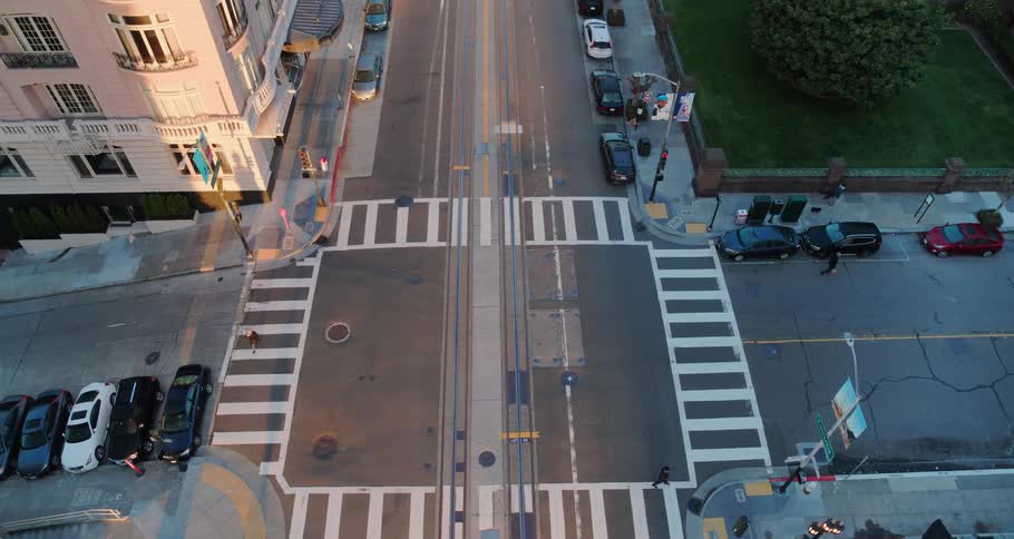 Pedestrians move along street near intersection as sun highlights corner of building