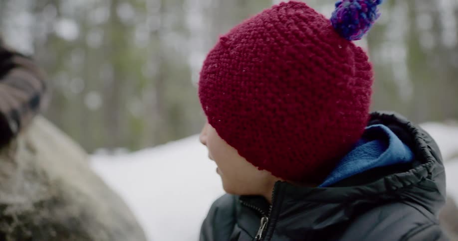 Father and son sitting on a rock sip at their tea in the snow covered forest