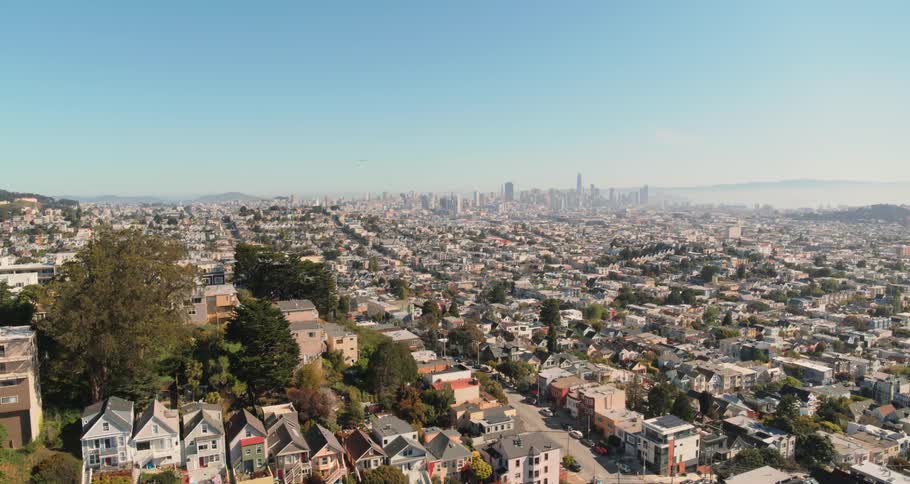 The rooftops and streets of neighborhood homes and apartments with a city skyline on the hazy horizon