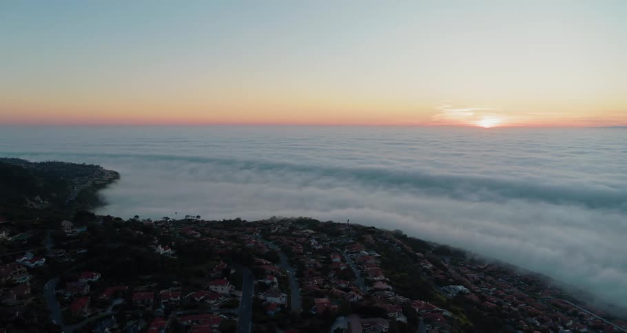 Sunlight peeking over a sea of clouds below a small town