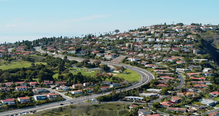 Vehicle traffic passes by a neighborhood that sits on and below hills