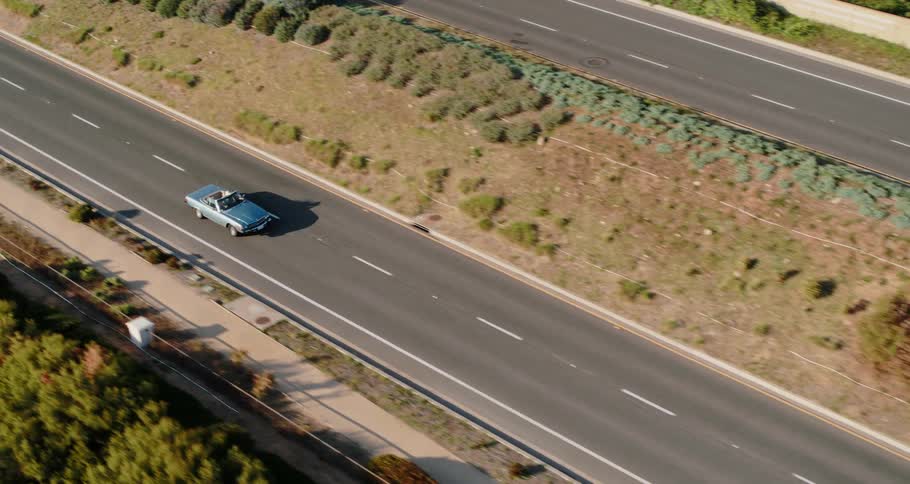 A blue convertible travels on a rural road on a sunny day