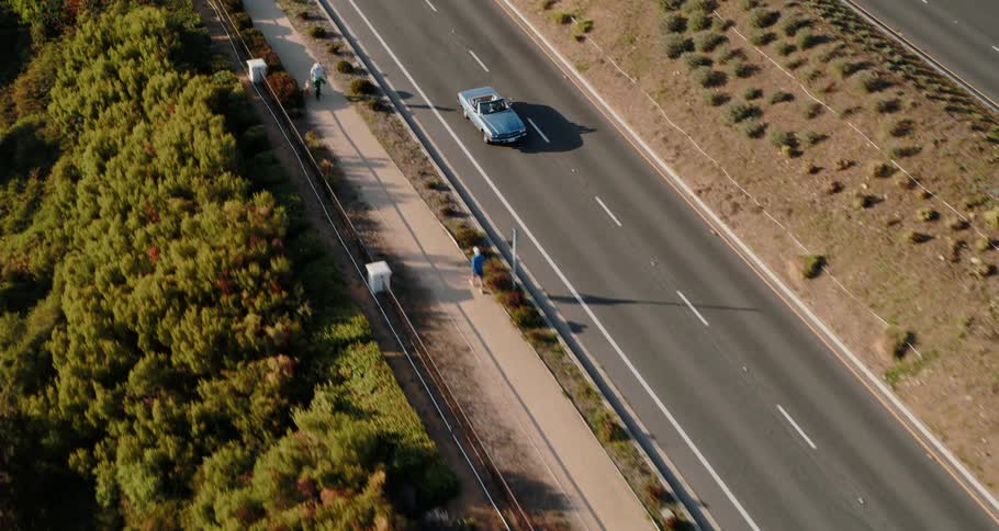 A blue convertible drives with its top down through a rural area