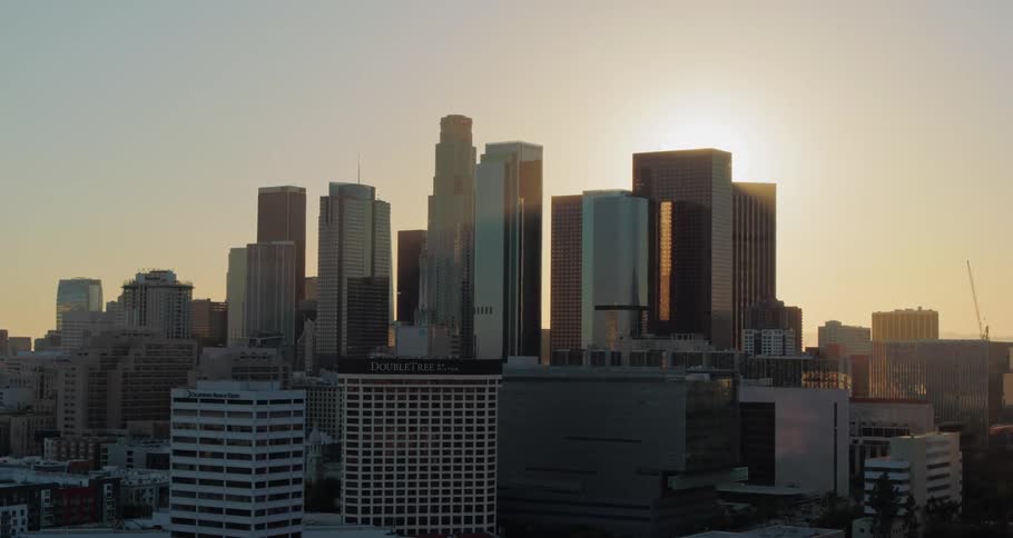 Aerial view of city skyline reveals the sun setting behind skyscrapers