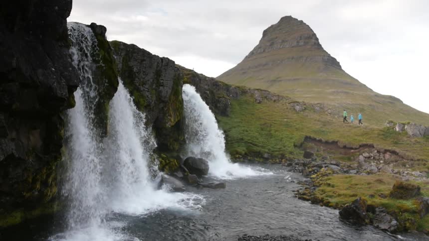 Three waterfalls are falling into the same place as people walk nearby