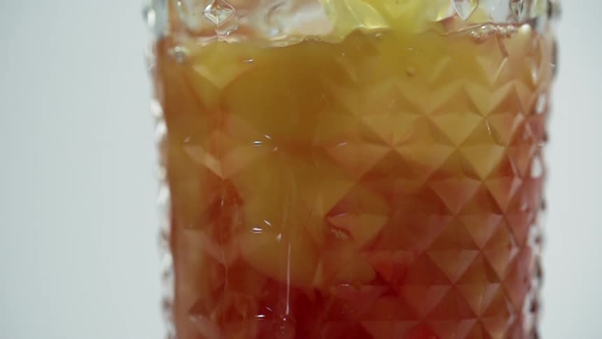 A yellow liquid being poured into a glass with ice