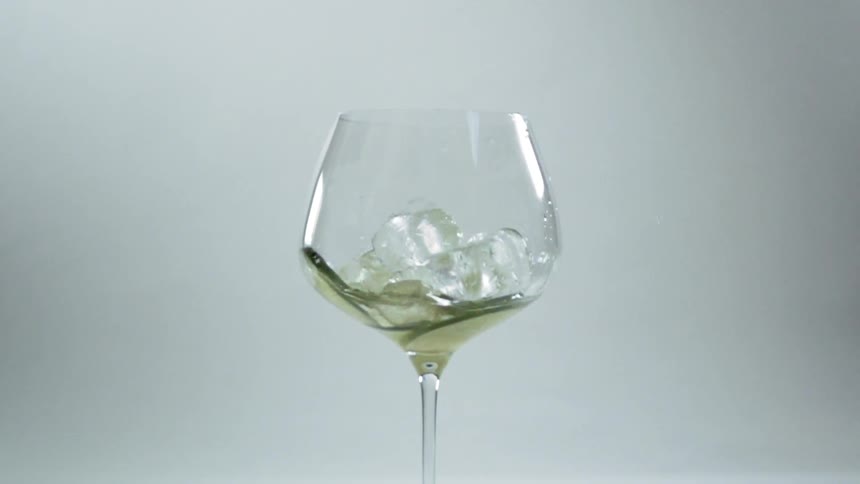 Ice cubes fall in to a wine glass with a drink in it