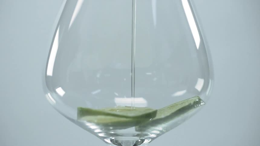 Liquid pours into a wine glass with lime slices