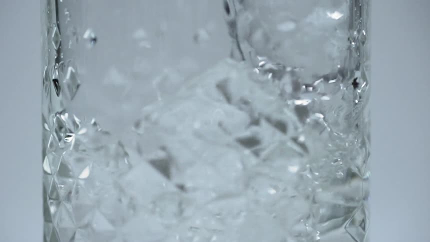 Ice cubes and water being stirred in a glass with a stirring spoon