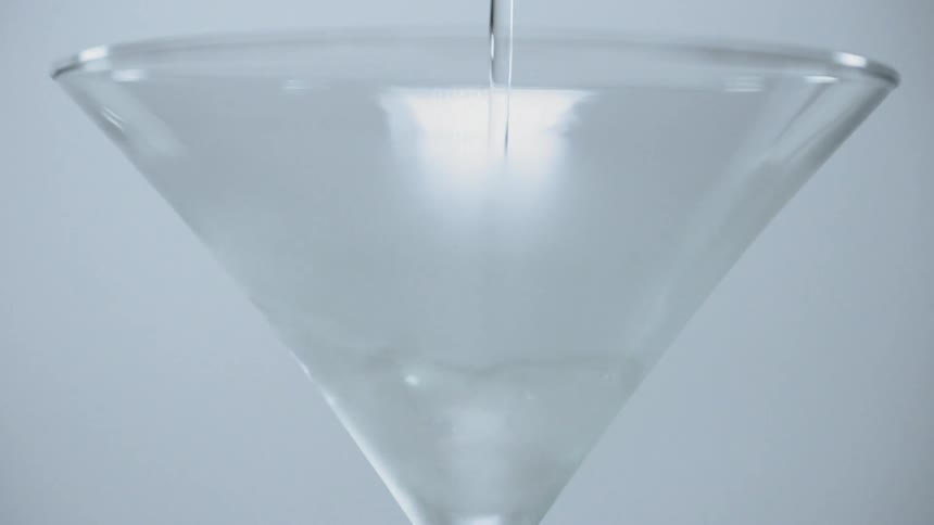A clear liquid being poured into a martini glass