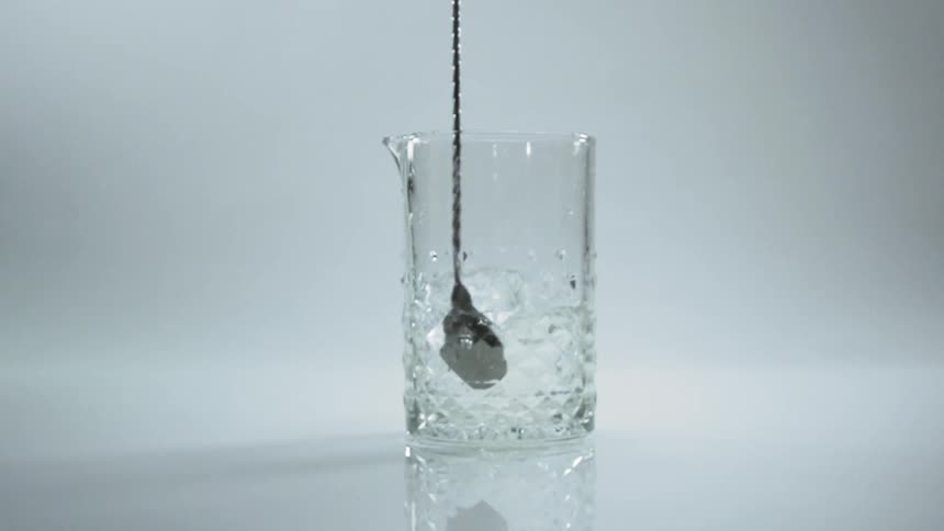 A stirrer moves an alcoholic drink around in a clear glass
