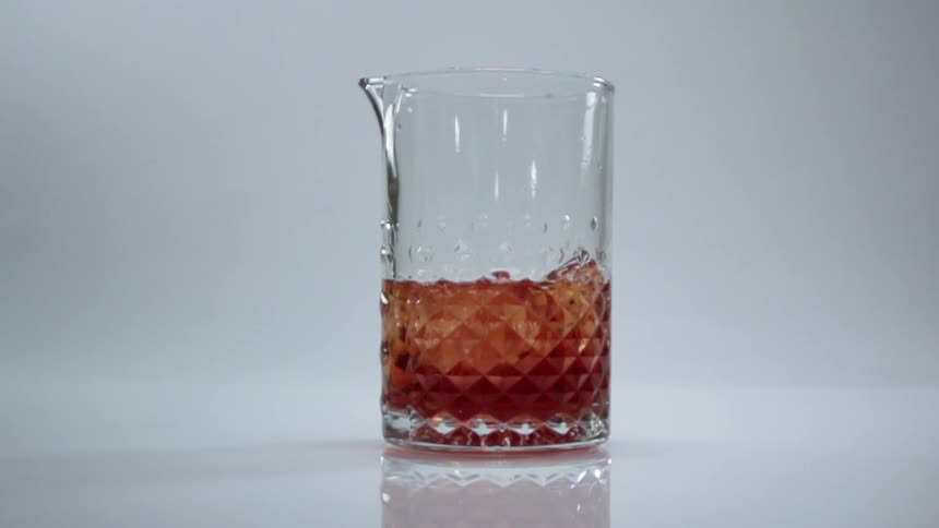 Amber liquid and ice cubes swirl in a clear glass mixing pitcher