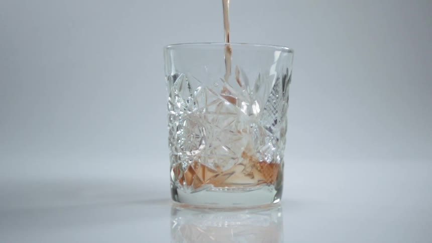 A cocktail is being poured into a glass full of ice cubes