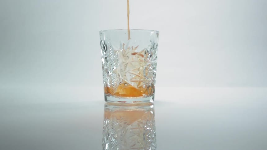 Orange liquor is poured in a short glass with textured cutouts