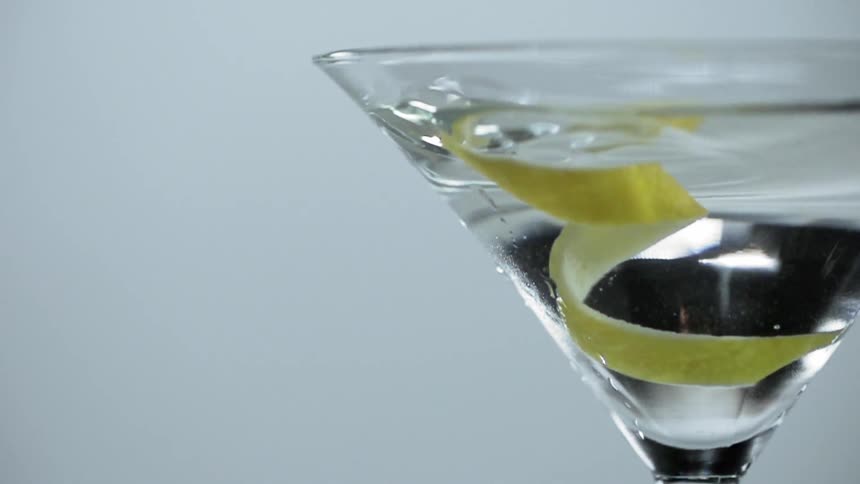 A lemon peel falling into a glass of martini