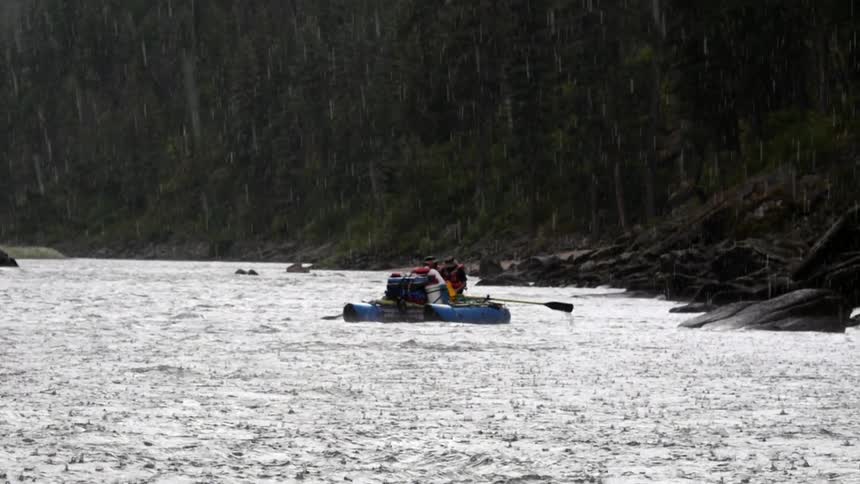 Three rafters paddle down a river in the rain