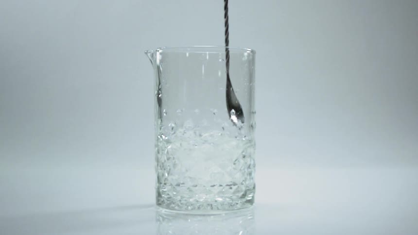 Long handled small spoon stirs ice and clear liquid in faceted pitcher