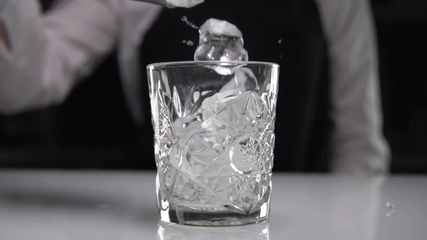 A woman drops ice off an ice scoop in to a cocktail glass