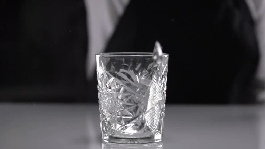 Bartender drops an big ice cube into a glass