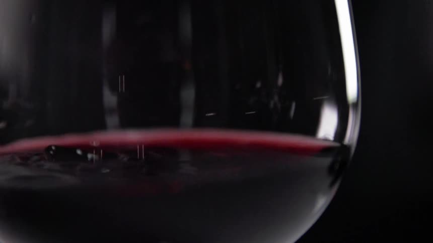 Close up of red wine drops falling slowly into wine glass partially filled with wine