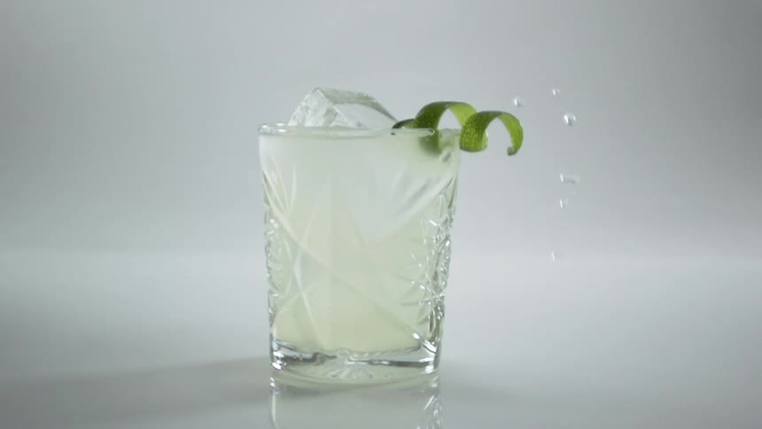 Lemon peel falls into glass of lemonade full of ice cubes