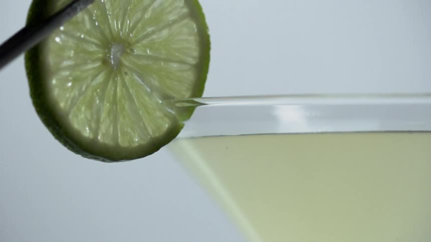 Lime with a slit being held by tweezers is gently being place on the rim of a full cocktail glass