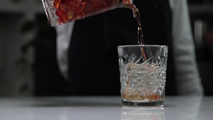 Bartender pouring cocktail drink from pitcher to crystal glass
