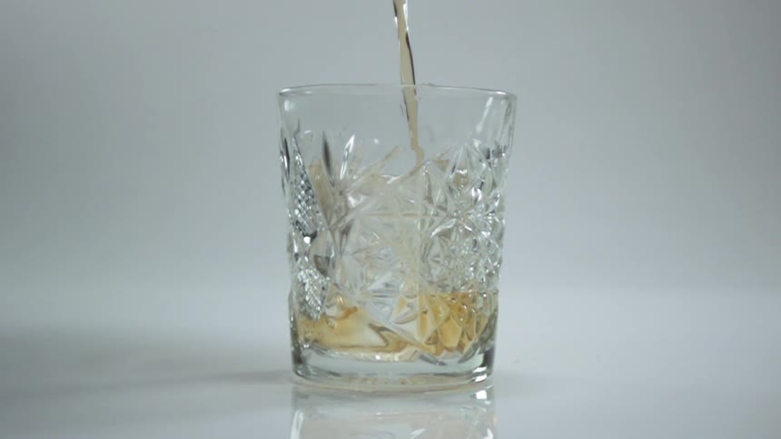 An amber liquid being poured in a drinking glass