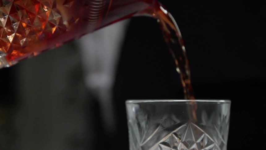 Liquor is being poured into a beveled glass at a bar