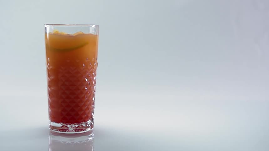 A slice of lemon falling into a drinking glass filled with ice and an amber liquid