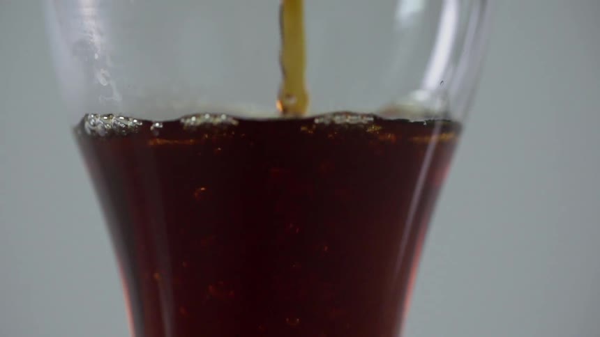 A dark brown liquor is poured in a tall glass