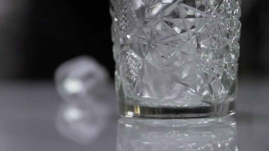Ice being poured into a glass and one ice cube falls on the table