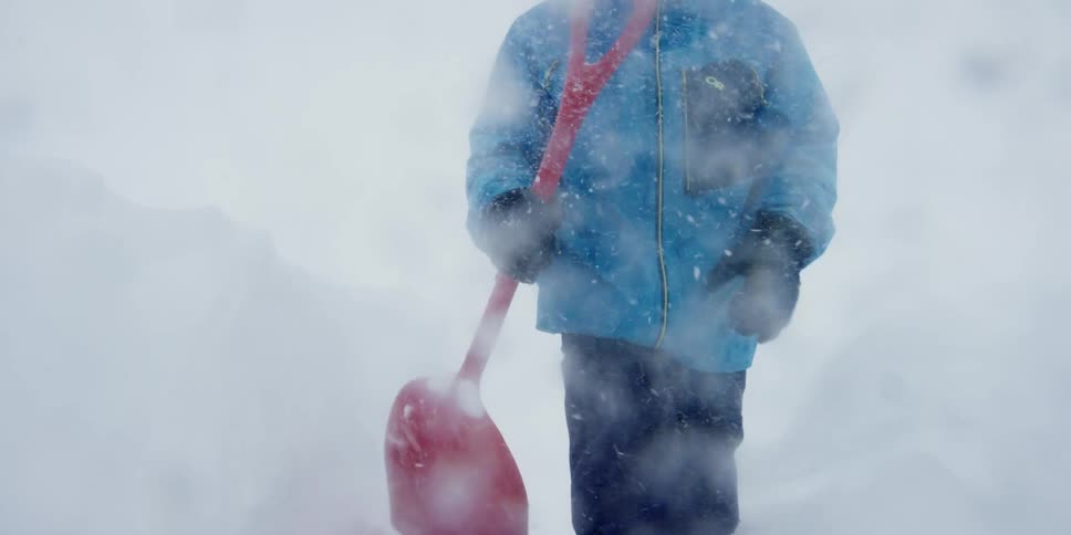 A man carrying a snow shovel walks through a blizzard