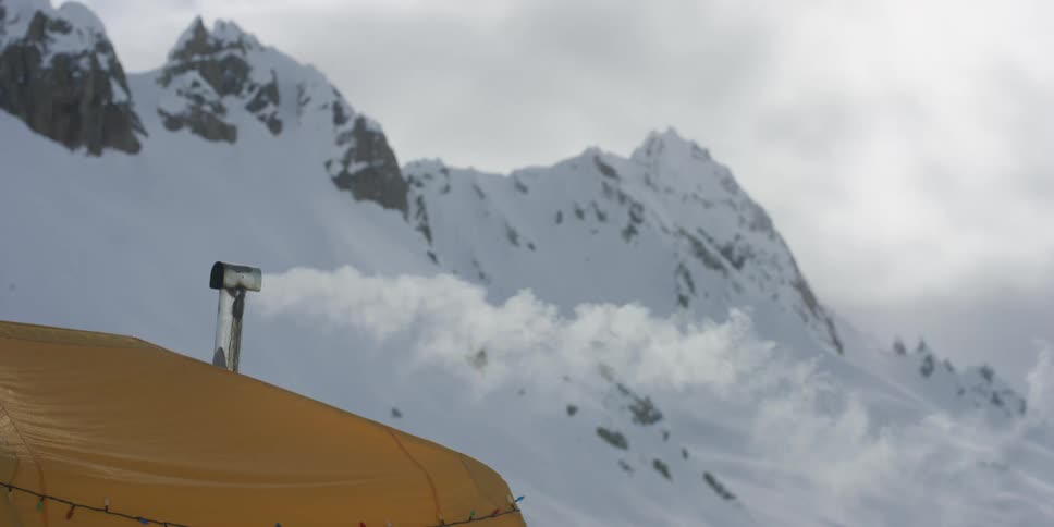 A chimney on top of a yellow tent with steam coming out of it with mountains and sky beyond