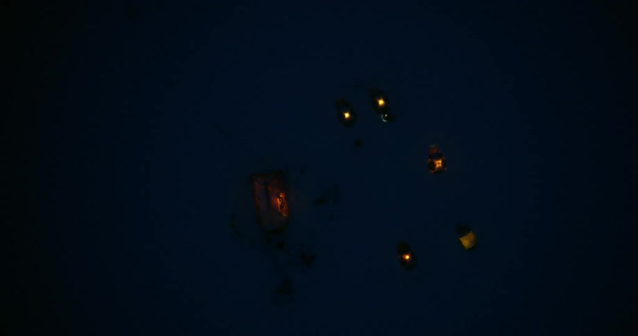 Aerial rising above a snowy camp of tents at night