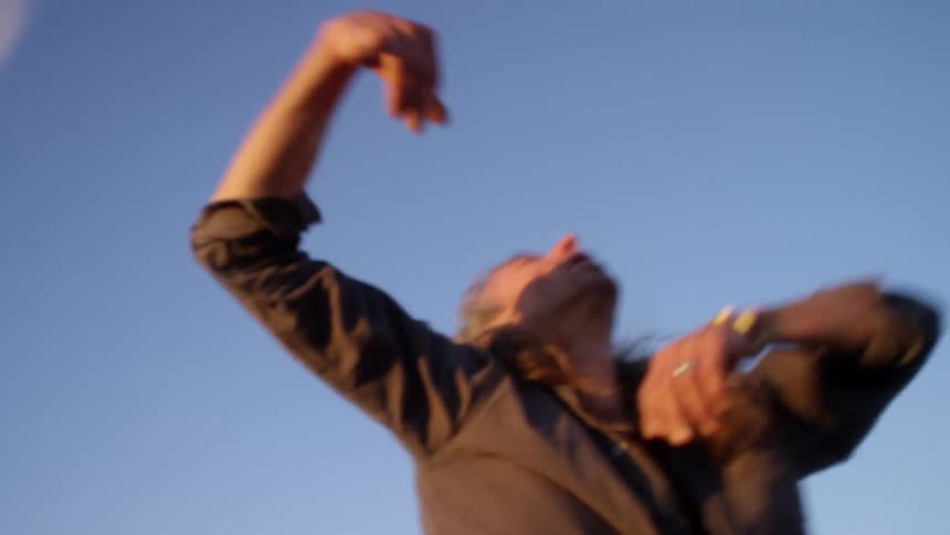 A man dances chaotically on a hillside in a desert