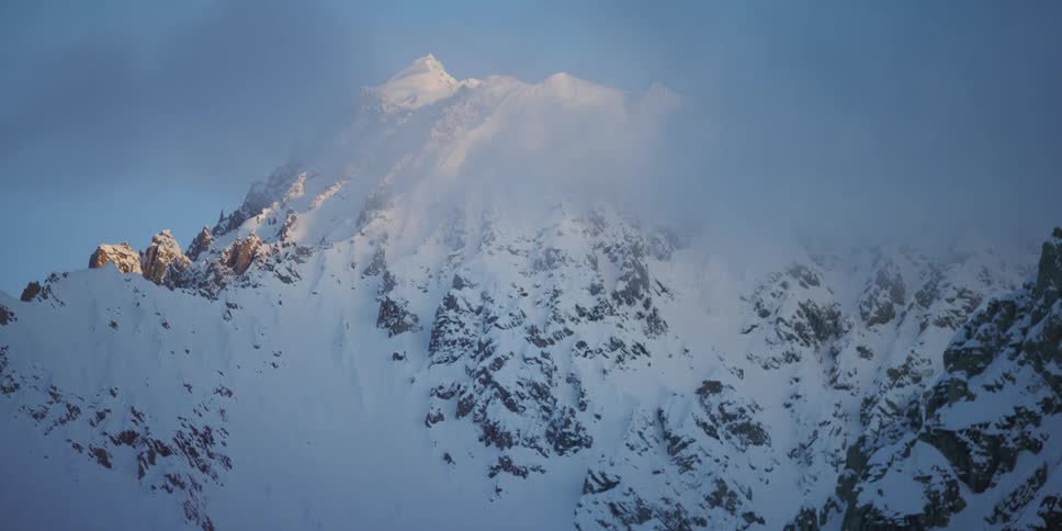 Sun highlights top of snow covered mountain peeking over clouds