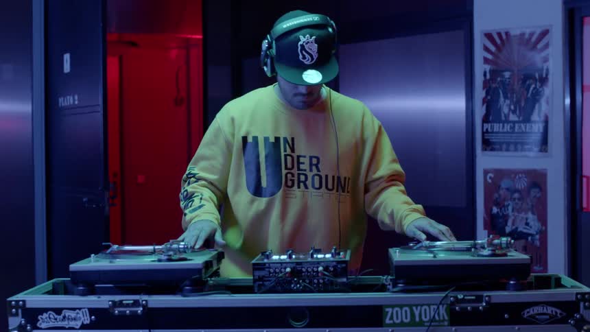 A man walking up to two turntables putting on headphones and scratching records