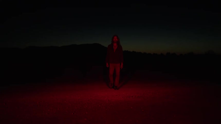 Man walks from dark spot to the red illuminated place in the field at night