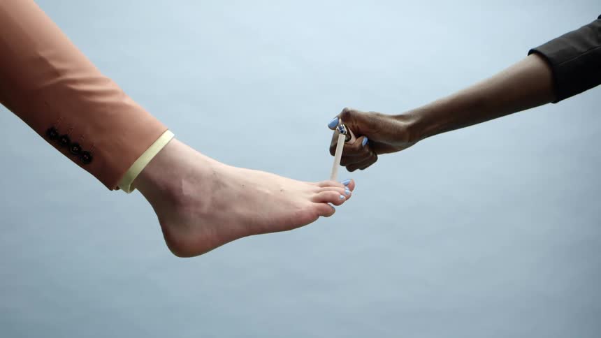 A foot holding a cigarette gets a light from someone