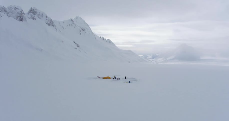 Aerial of people at their campsite at the base of a snowy mountain