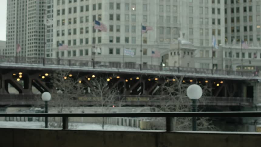 A city view of high rises and a bridge lined with flags slowly rolls by