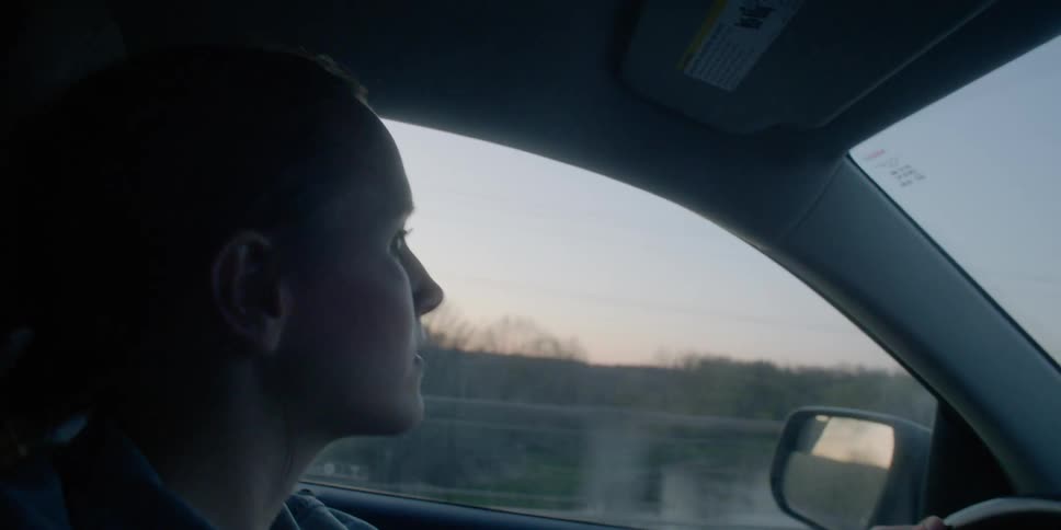 A young woman drives in a car and glances out the window