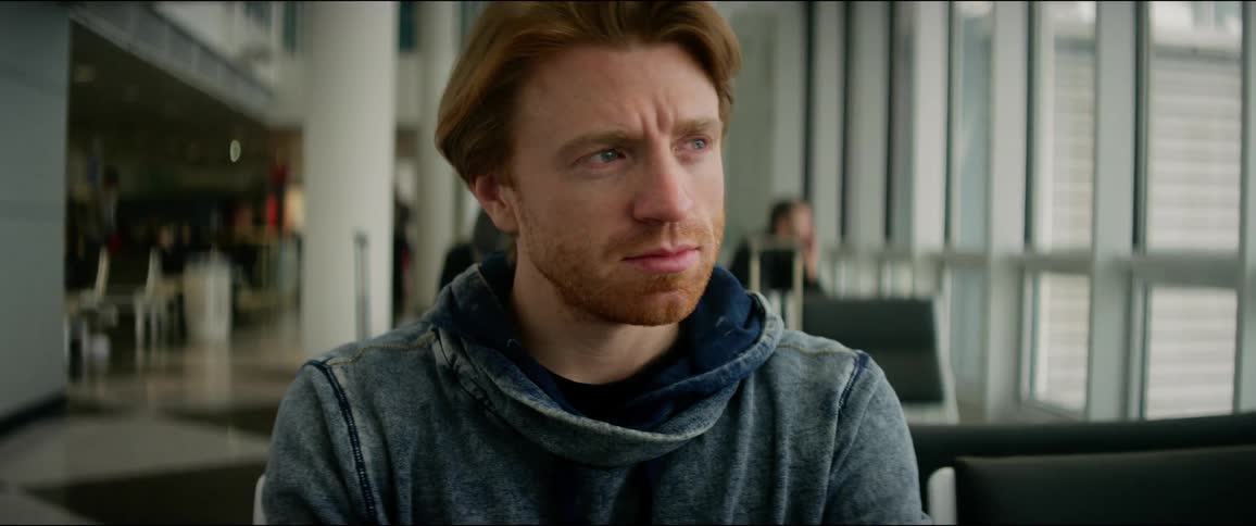 A man sits with his arms crossed in a terminal looking out the window